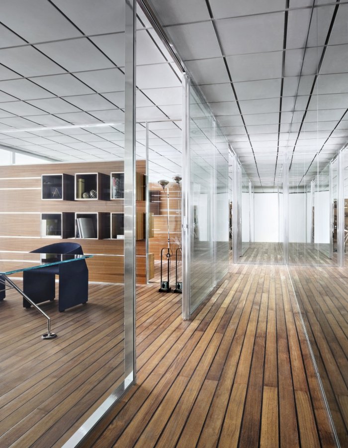 Executive office behind glass partitions: glass-top desk, blue armchairs and wood-panelled wall