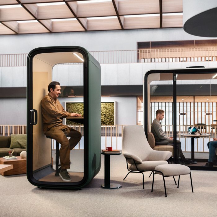Two-person acoustic meeting pod on an open-plan London office floor, occupant on a video call behind the glazed door